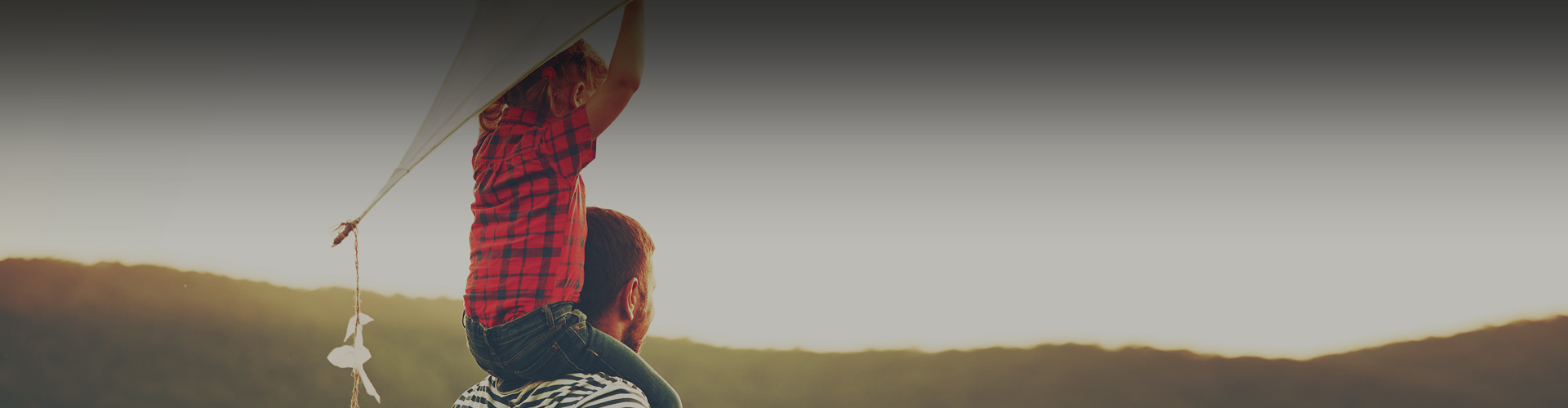 Photo of a young boy holding a kite while sitting on his dad's shoulders