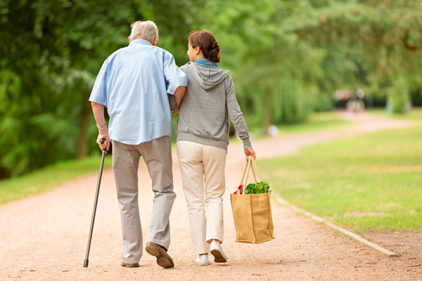 Photo of healthcare worker helping an elderly man walk with groceries