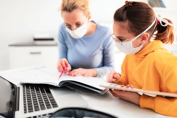 A photo of a teacher and a student reviewing study materials while wearing masks